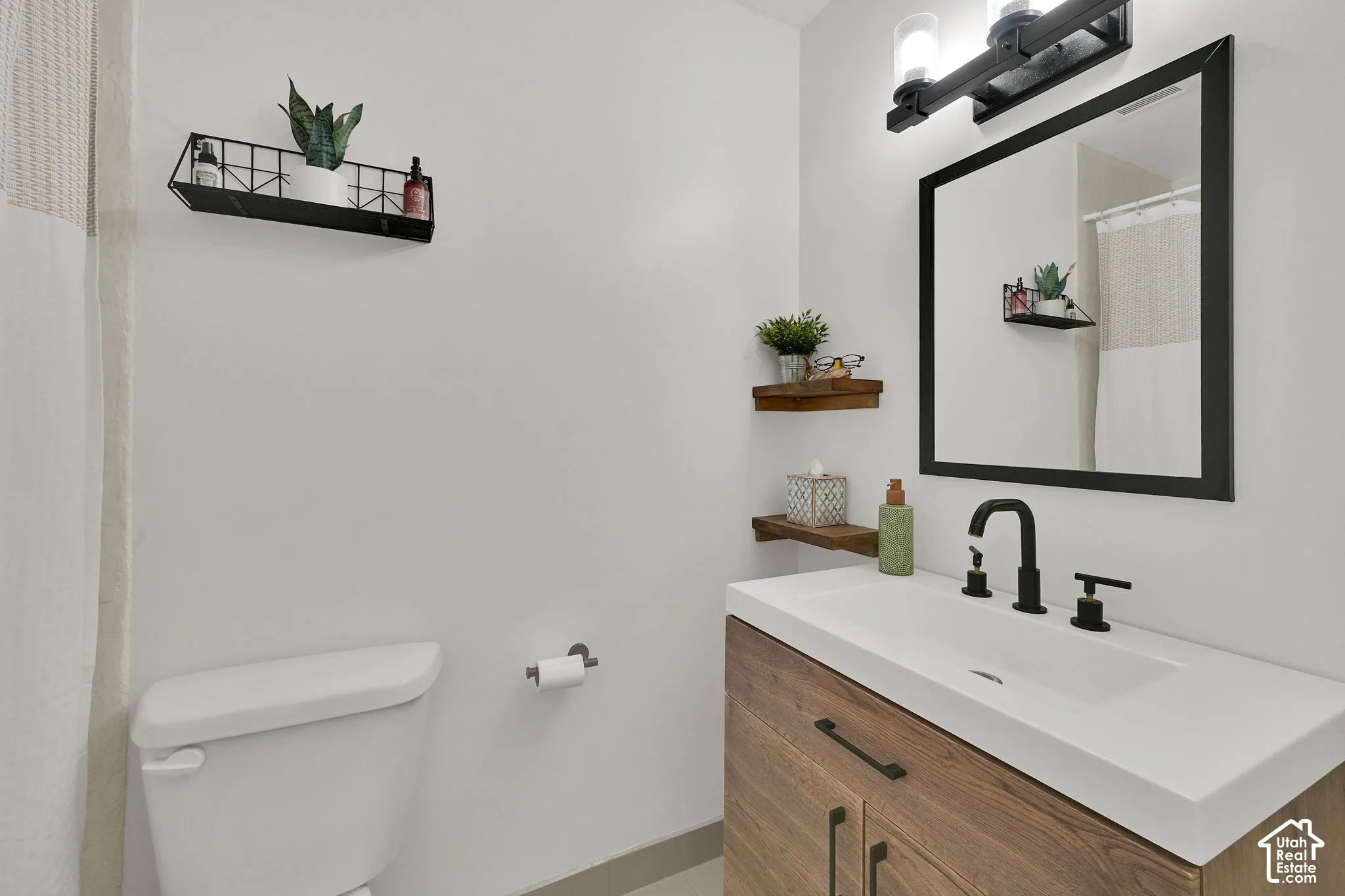 Main floor Bathroom. Wood-finish vanity with an integrated white sink, matte black faucet, and a framed mirror