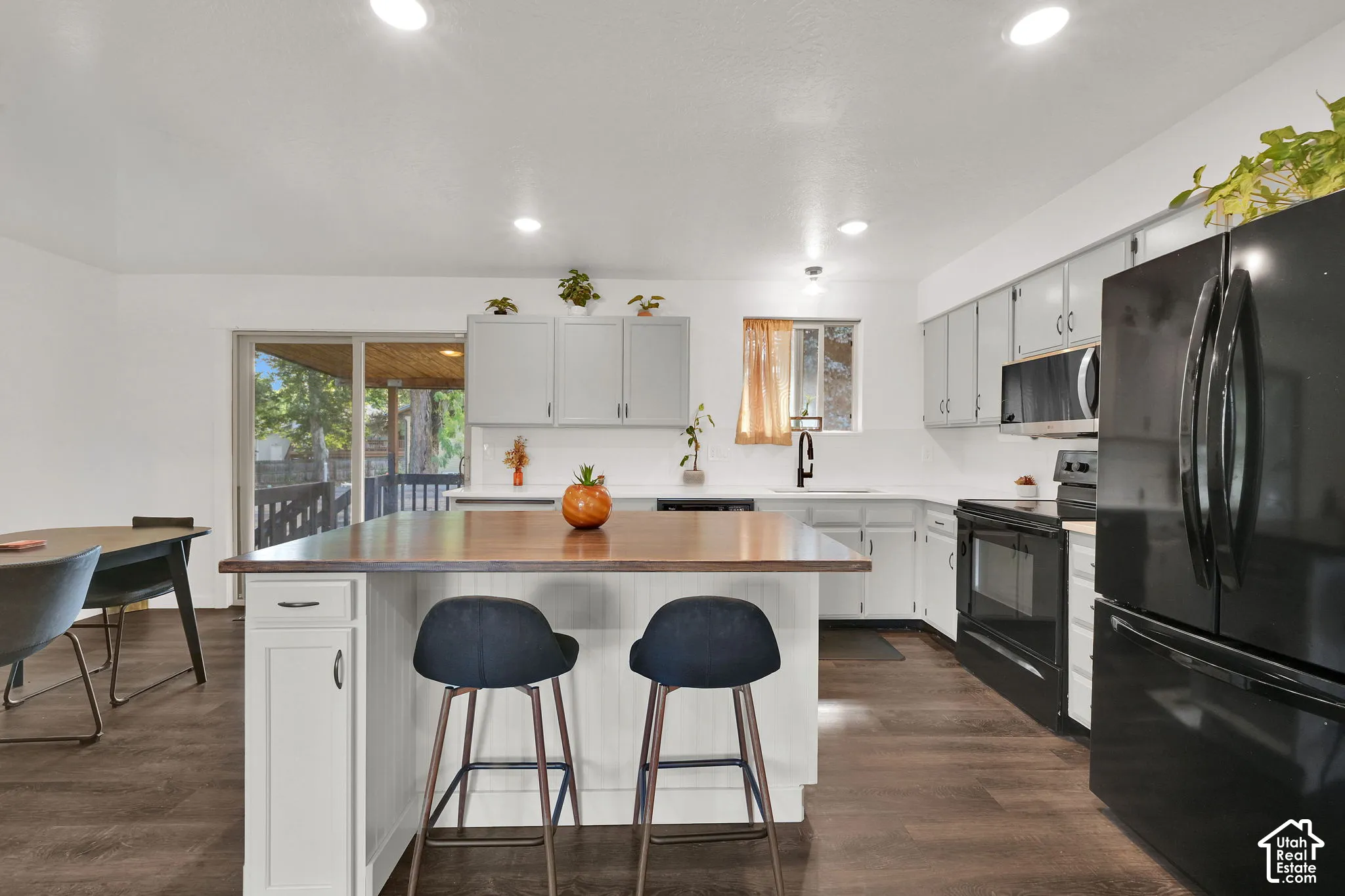 Kitchen featuring an island with wood-finish countertop, white cabinetry with dark hardware, recessed lighting, wood-finish flooring, and a sliding glass door