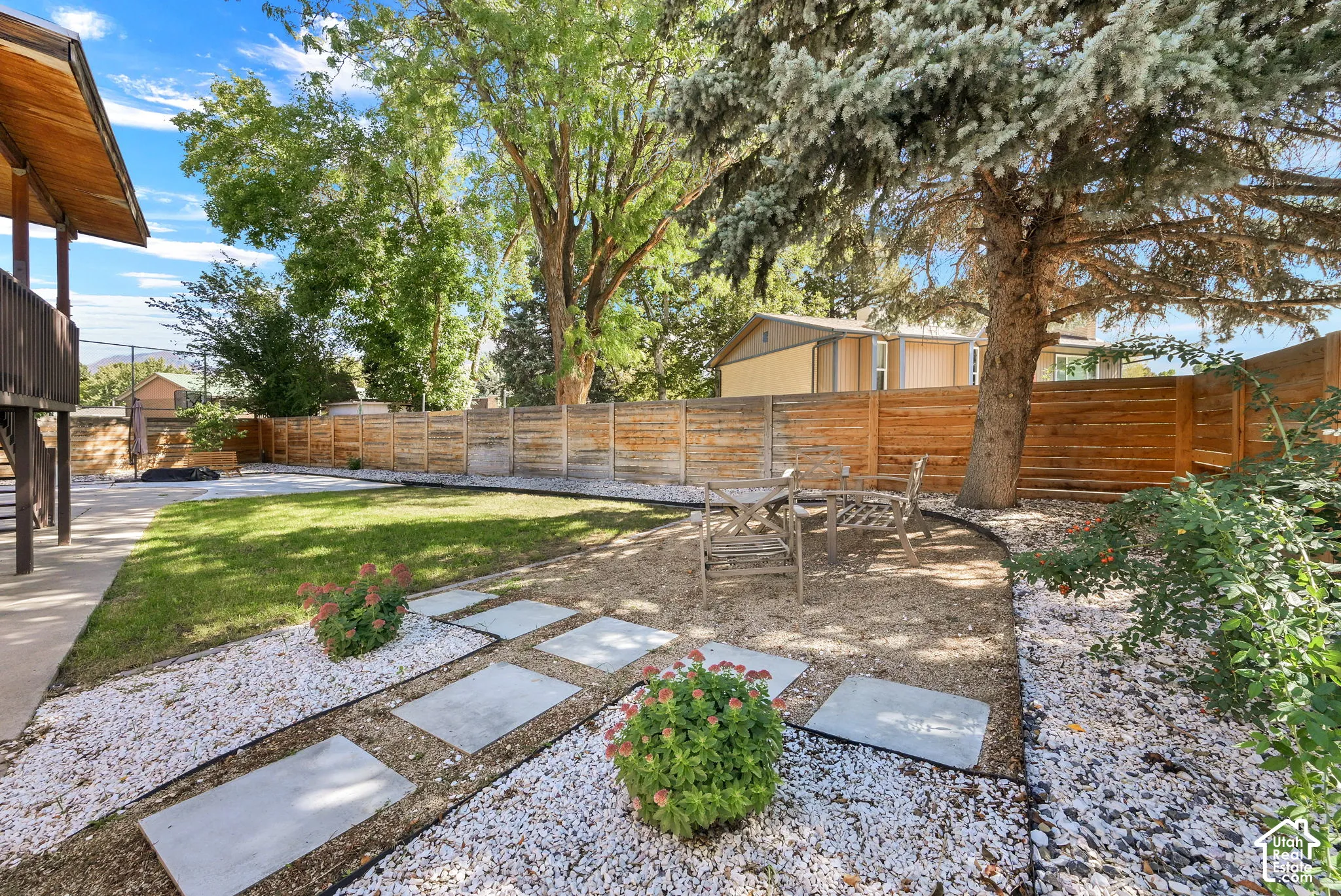 Expansive backyard featuring a manicured lawn, established perimeter fencing, concrete stepping stones, and mature trees