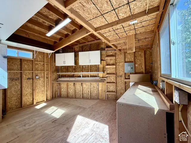 Exposed wood beam ceiling, plywood flooring, built-in workbench, wall-mounted cabinetry,  large window, and power.