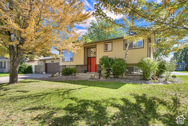 Split-level residence featuring a vibrant red entry door, an attached two-car garage, and mature landscaping
