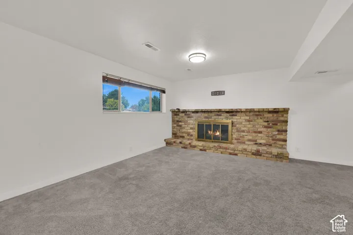 Brick fireplace with a brass firebox, flush-mount ceiling light, white walls, and gray carpeting