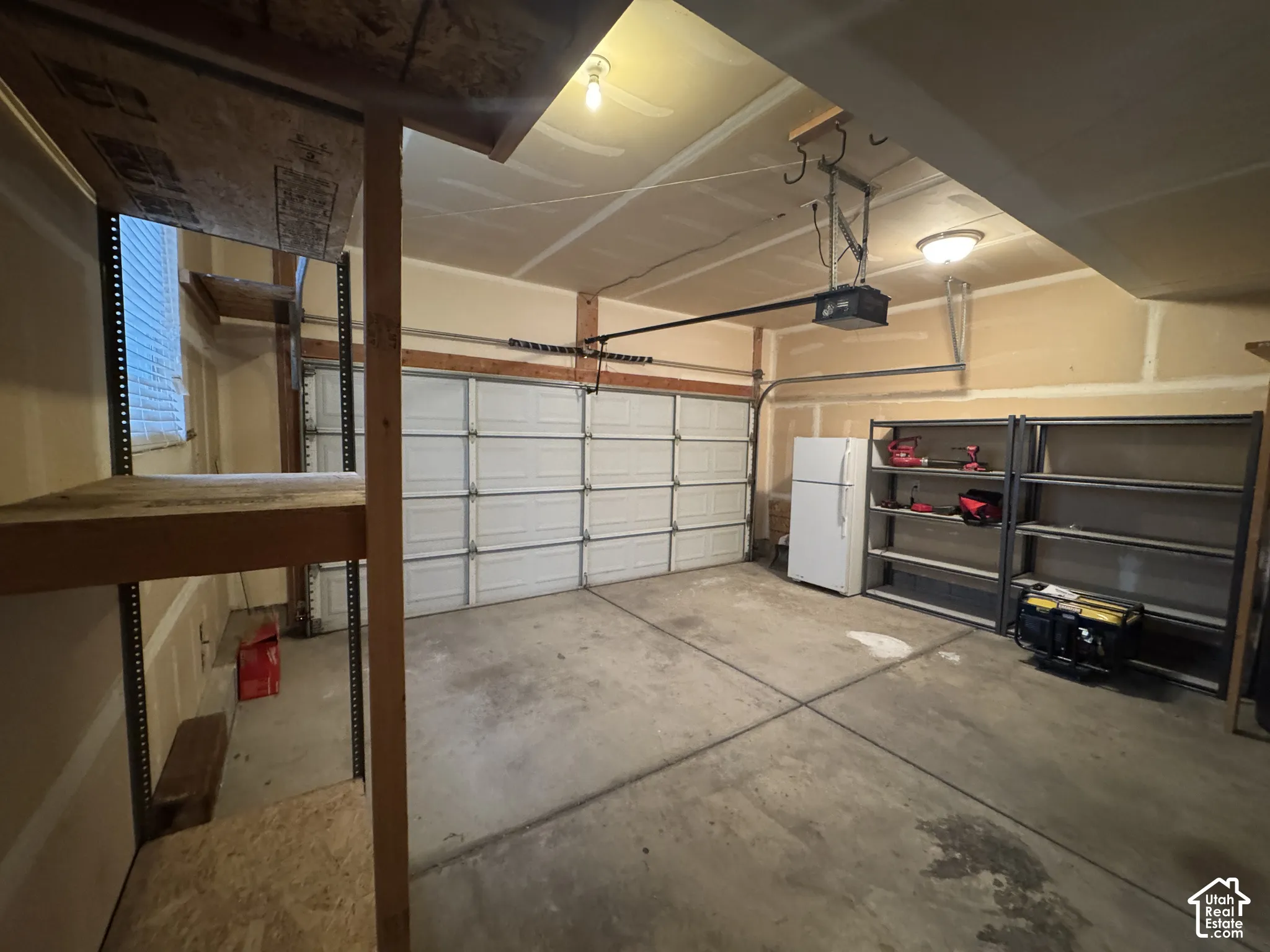 Large Garage: Concrete flooring with built-in overhead storage, interior shelving, and a roll-up garage door