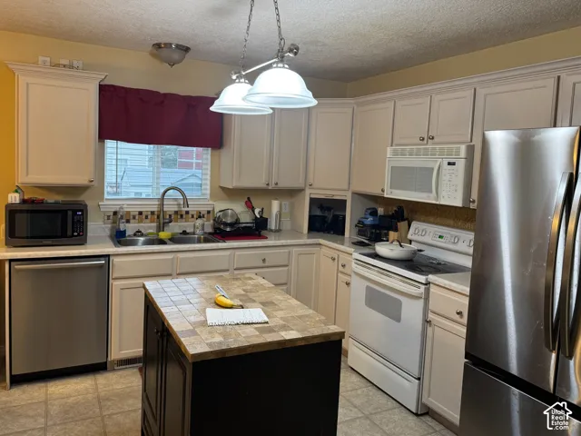 Kitchen featuring light-toned cabinetry, a tiled center island, and stainless steel appliances including a refrigerator and dishwasher