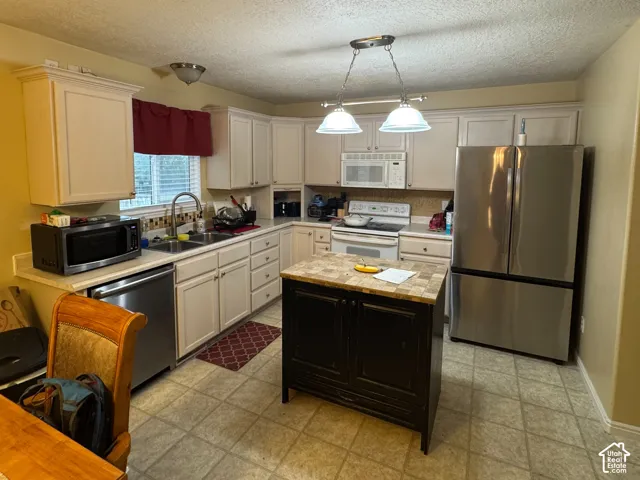 Kitchen featuring white cabinetry, stainless steel appliances, a center island with a tiled countertop, and light-toned flooring