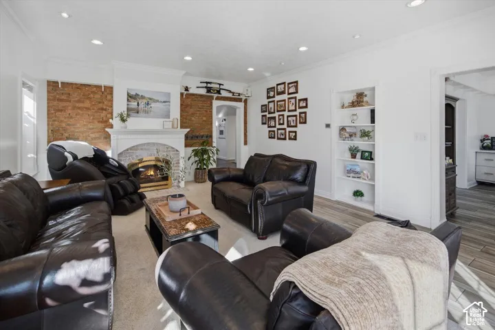 Living area featuring an exposed brick accent wall, recessed lighting, a fireplace with a white mantel, and built-in shelving