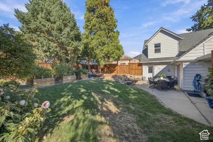 Expansive green lawn, concrete patio, raised garden beds, wood fencing, and mature trees