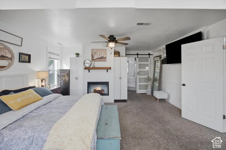 Warm carpeted flooring, a ceiling fan, a built-in fireplace, and a sliding barn door with frosted glass panels