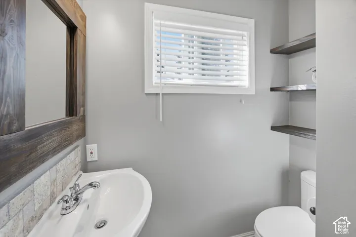 White pedestal sink with chrome faucet, wood-framed mirror, and a tiled backsplash