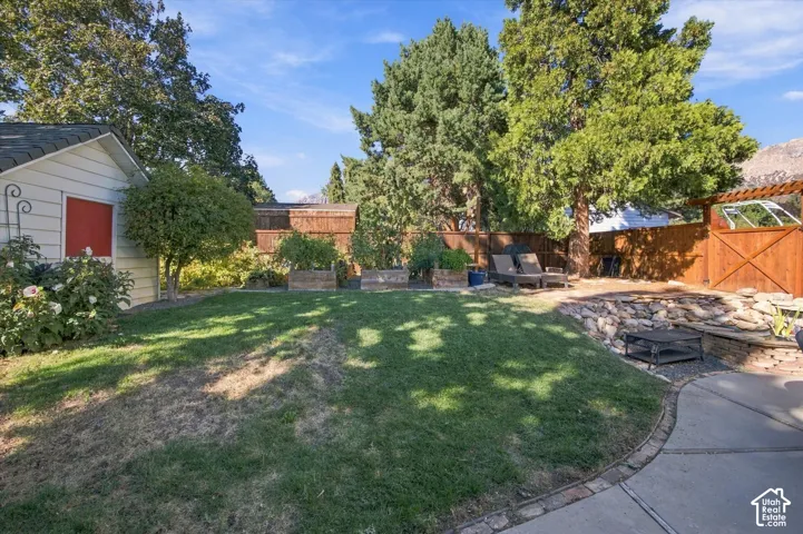 Expansive lawn area, privacy fencing, concrete patio with brick border, garden shed, and raised planter beds