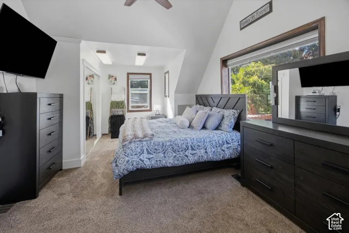 Vaulted ceiling, ceiling fan, carpet flooring, a large window, and mirrored closet doors