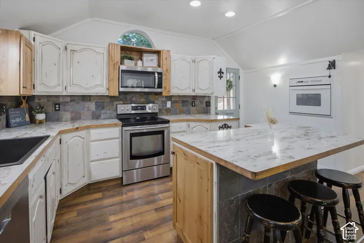 Vaulted ceilings, wood-finish flooring, stone tile backsplash, stainless steel appliances, and a built-in oven