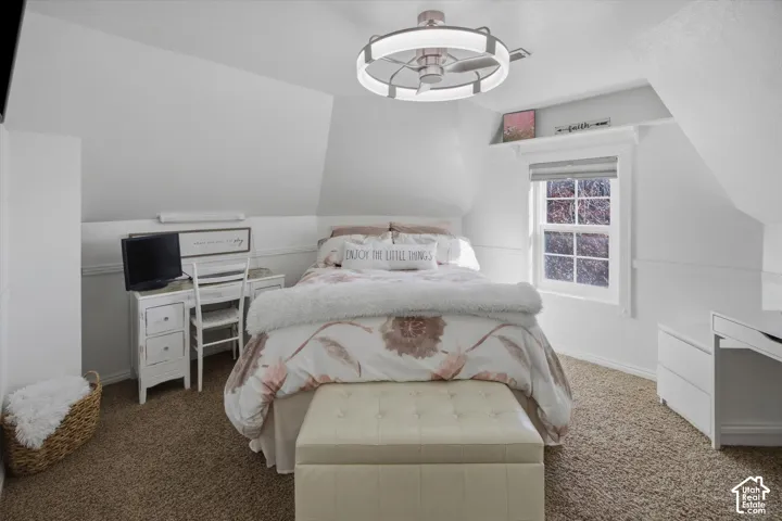 Carpeted flooring, vaulted ceiling, ceiling fan with integrated lighting, window with trim, and built-in shelving