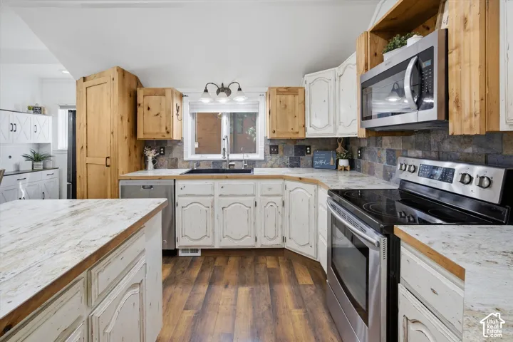 Stainless steel appliances, wood-finish flooring, white and natural wood cabinetry, light-toned countertops, and a tiled backsplash