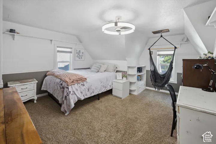 Carpeted flooring, vaulted ceiling, built-in shelving, ceiling fan with integrated lighting, and multiple windows