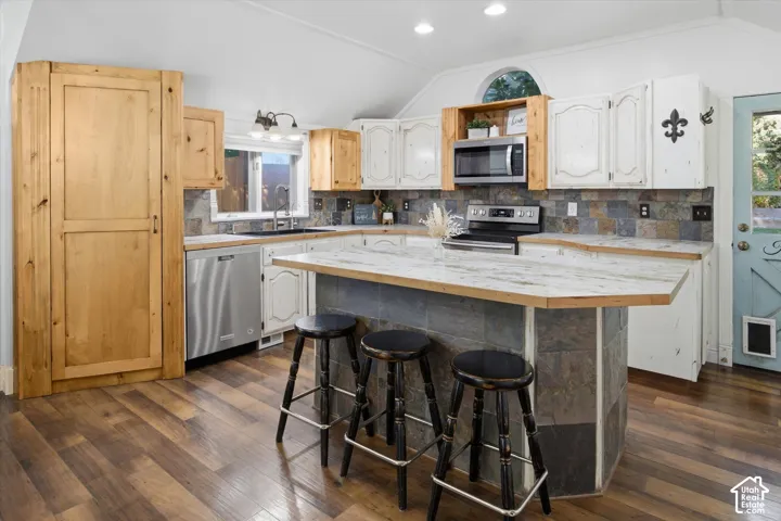 Vaulted ceiling, wood-finish flooring, two-tone cabinetry, stainless steel appliances, and a stone tile backsplash