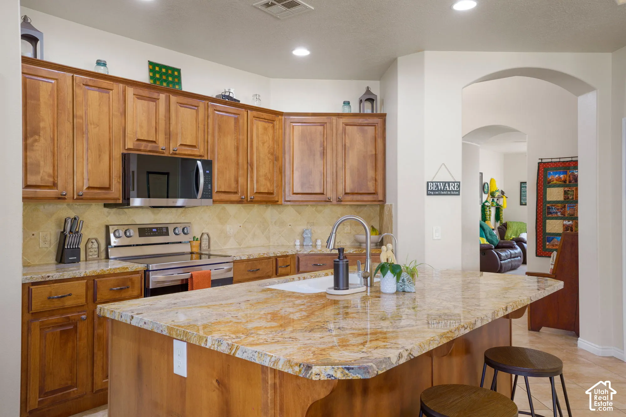 Spacious kitchen featuring a large island with an integrated sink, rich wood cabinetry, and stainless steel appliances including an oven and microwave