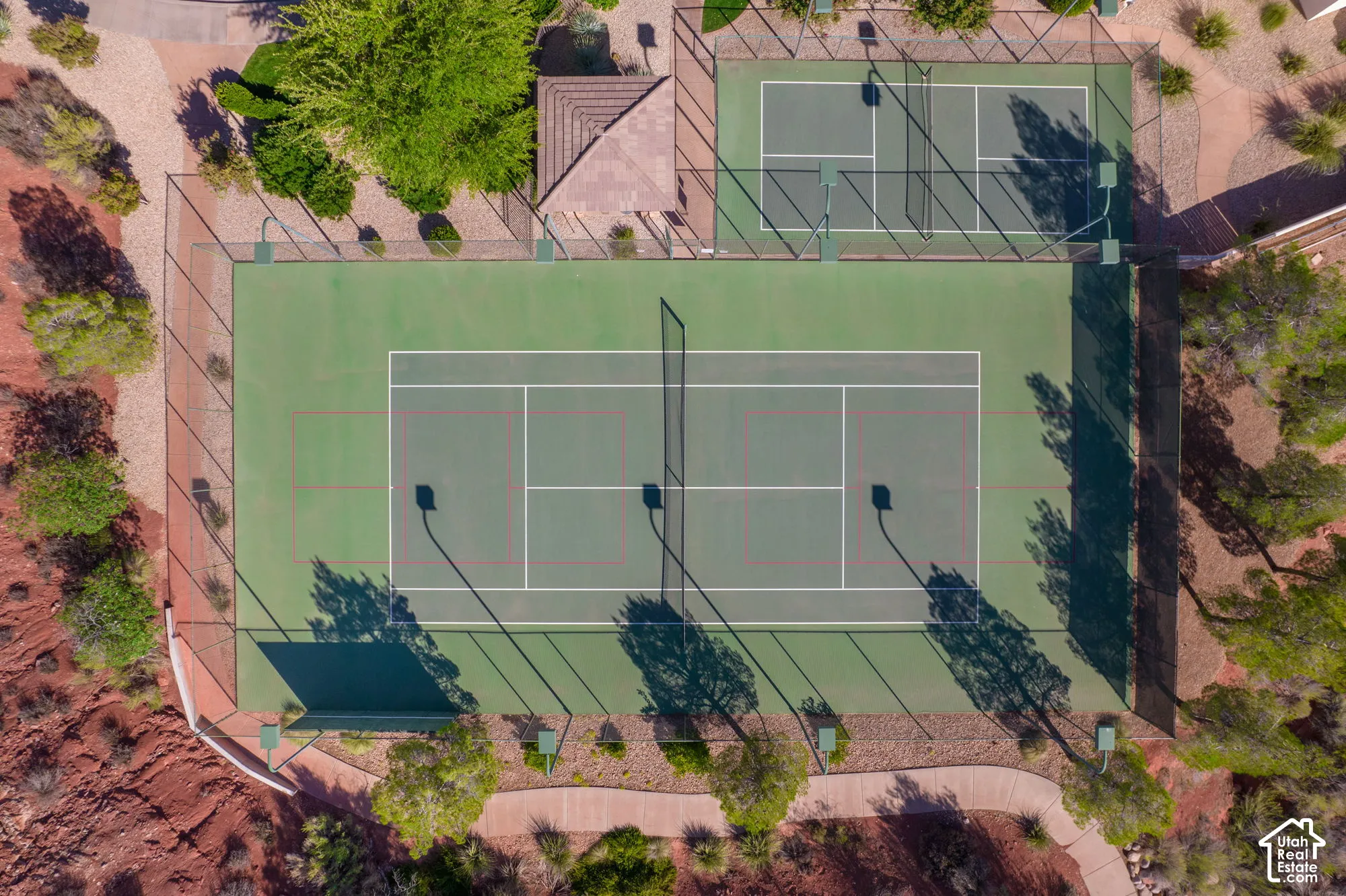 Two full-sized tennis courts with chain-link fencing, surrounded by paved pathways and desert landscaping