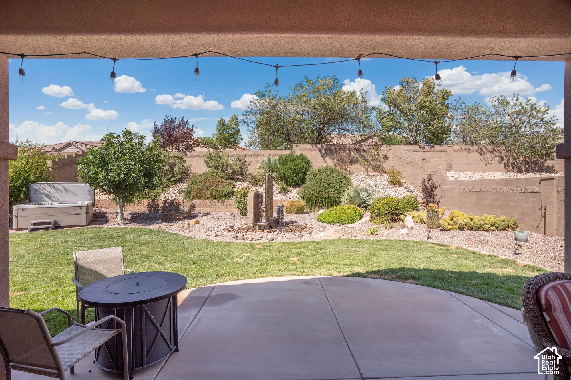 Covered patio with string lighting, curved concrete patio, and a grassy lawn