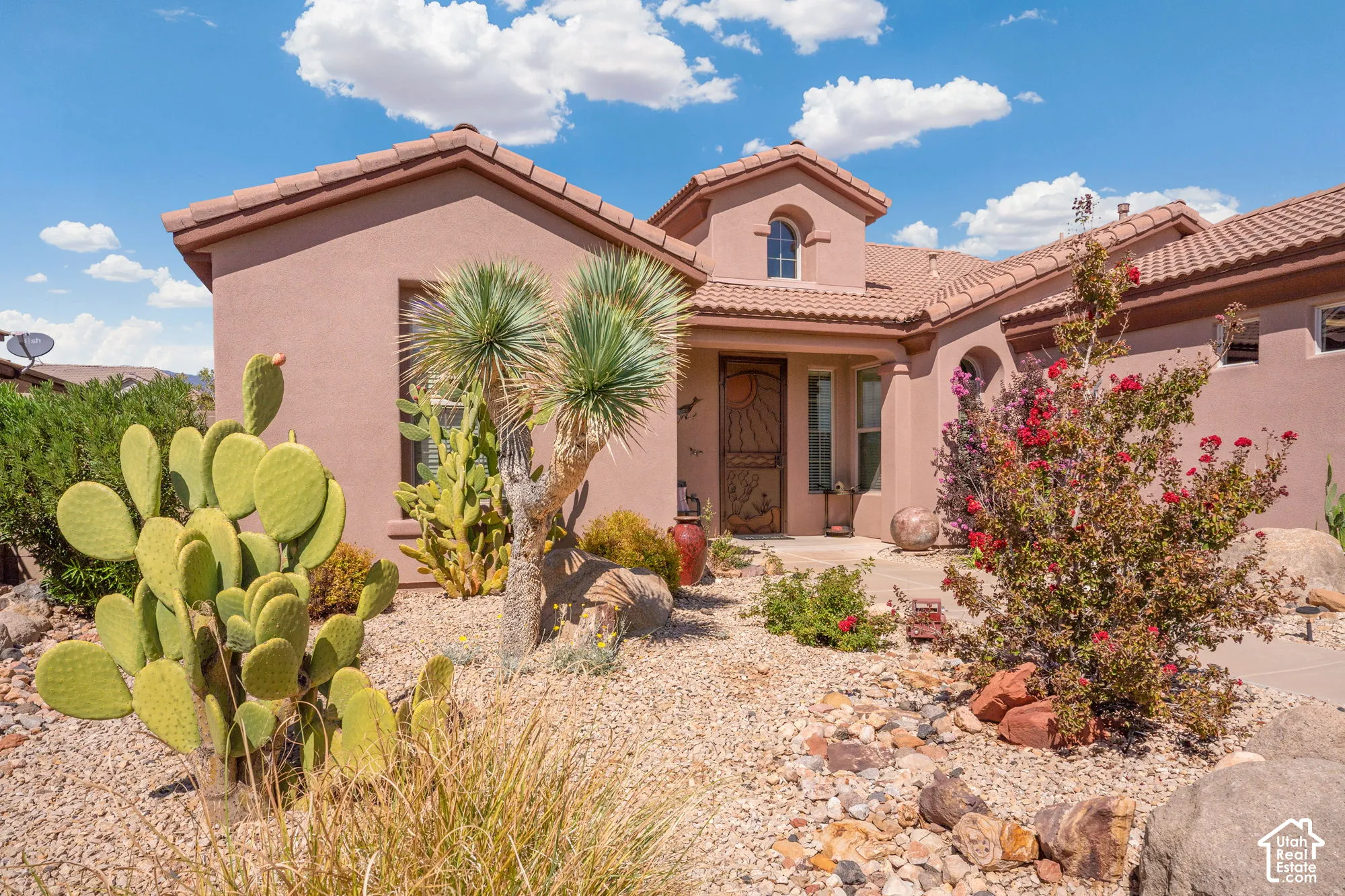 Southwestern style architecture with a stucco exterior, tile roof, arched entryway, and desert landscaping
