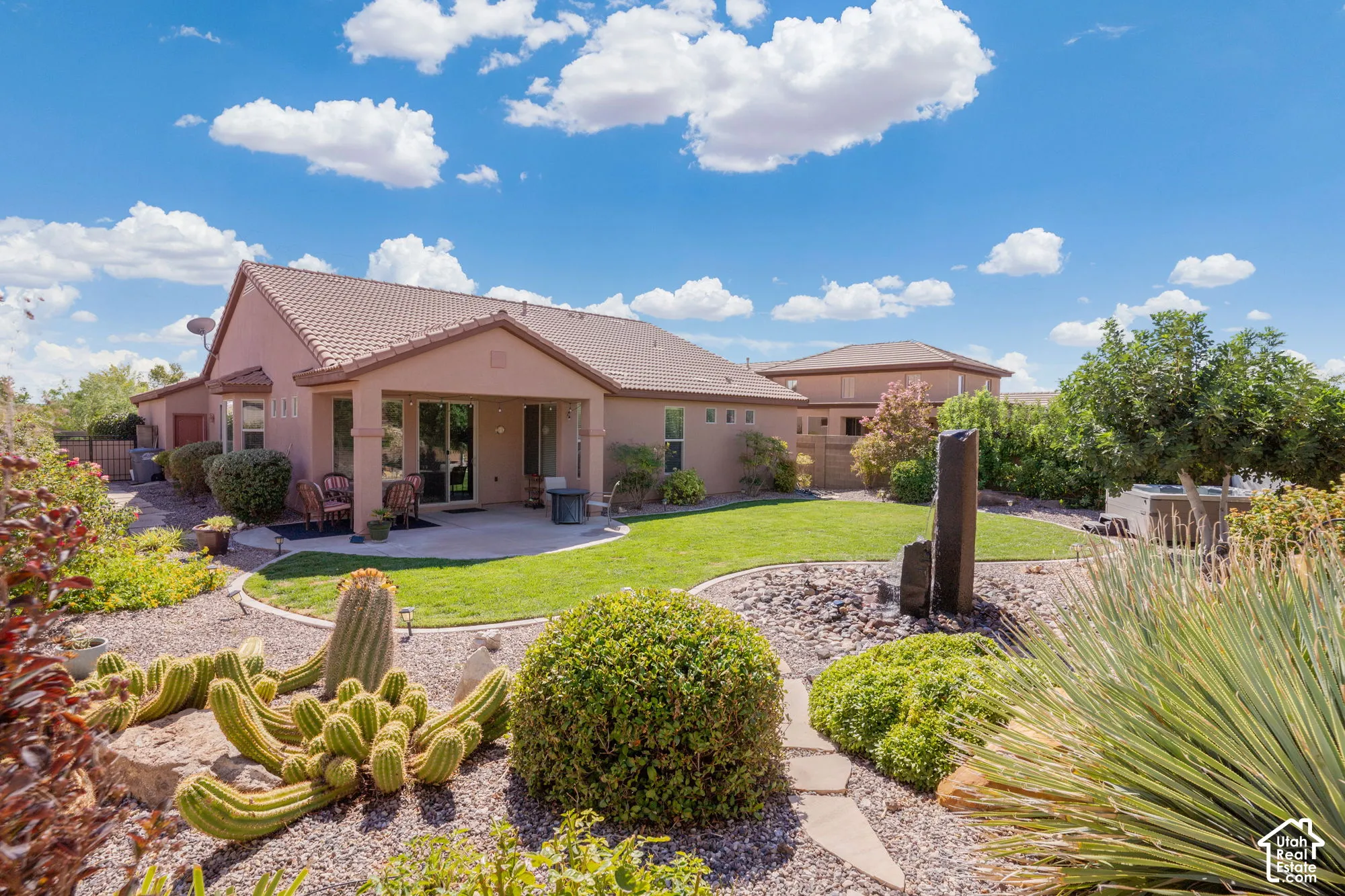 Expansive backyard featuring a manicured lawn, established desert landscaping with stone pathways, and a covered patio area with a concrete surface