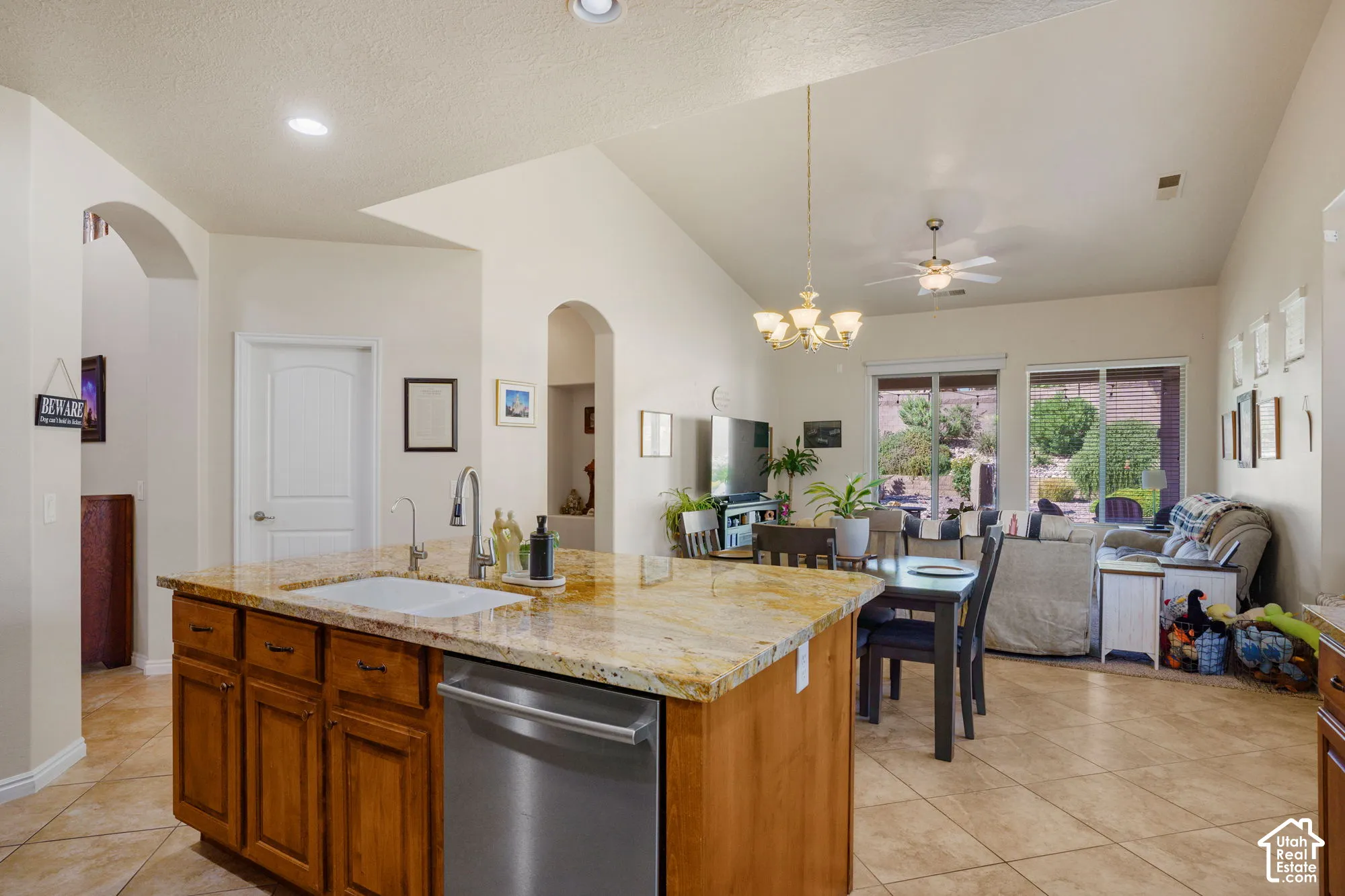 Spacious kitchen island with granite countertop and integrated sink, stainless steel dishwasher, vaulted ceilings, tiled flooring, and multiple sliding glass doors