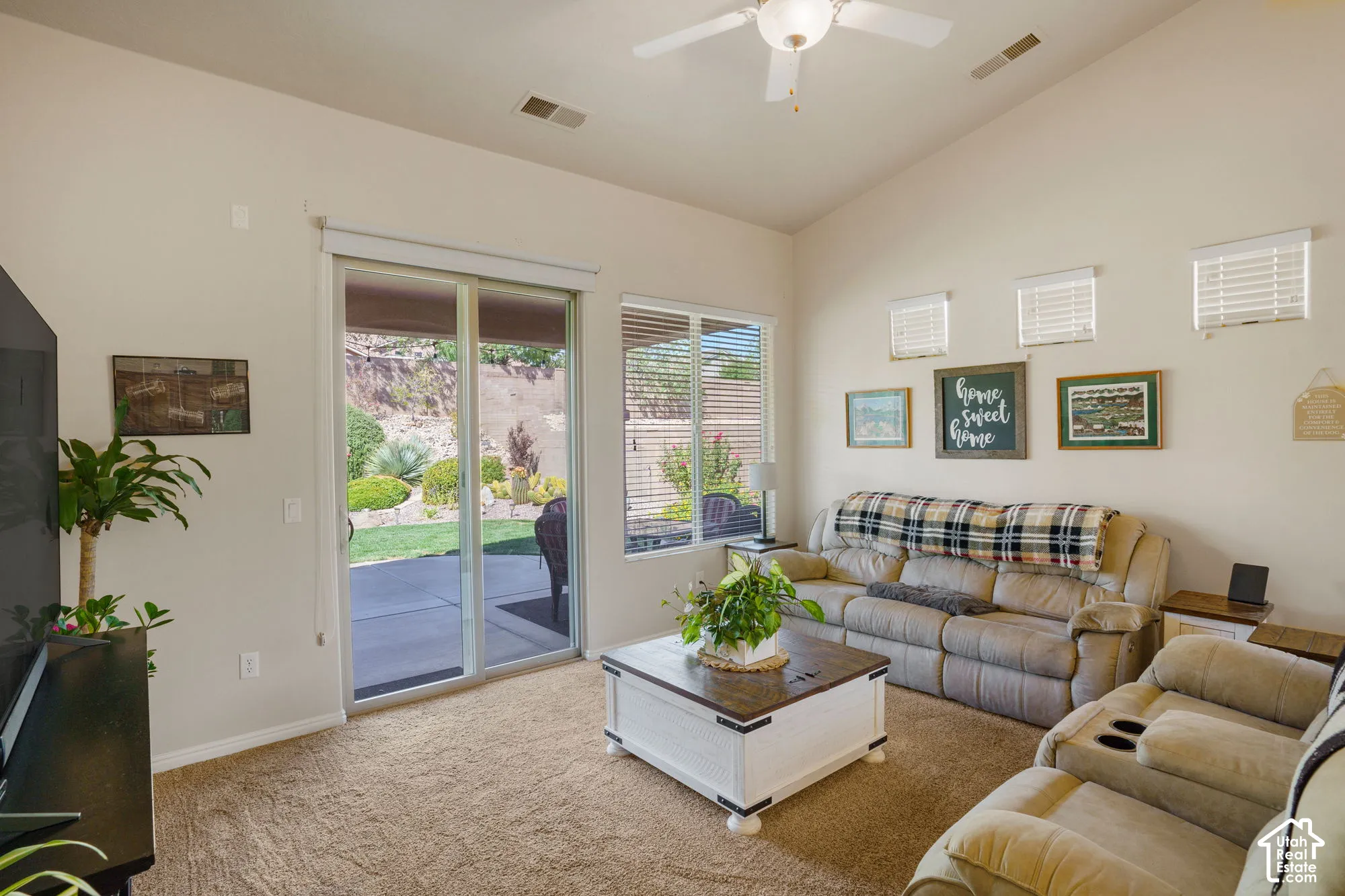 Vaulted ceiling with an attached ceiling fan, sliding glass door, and a private patio with landscaping