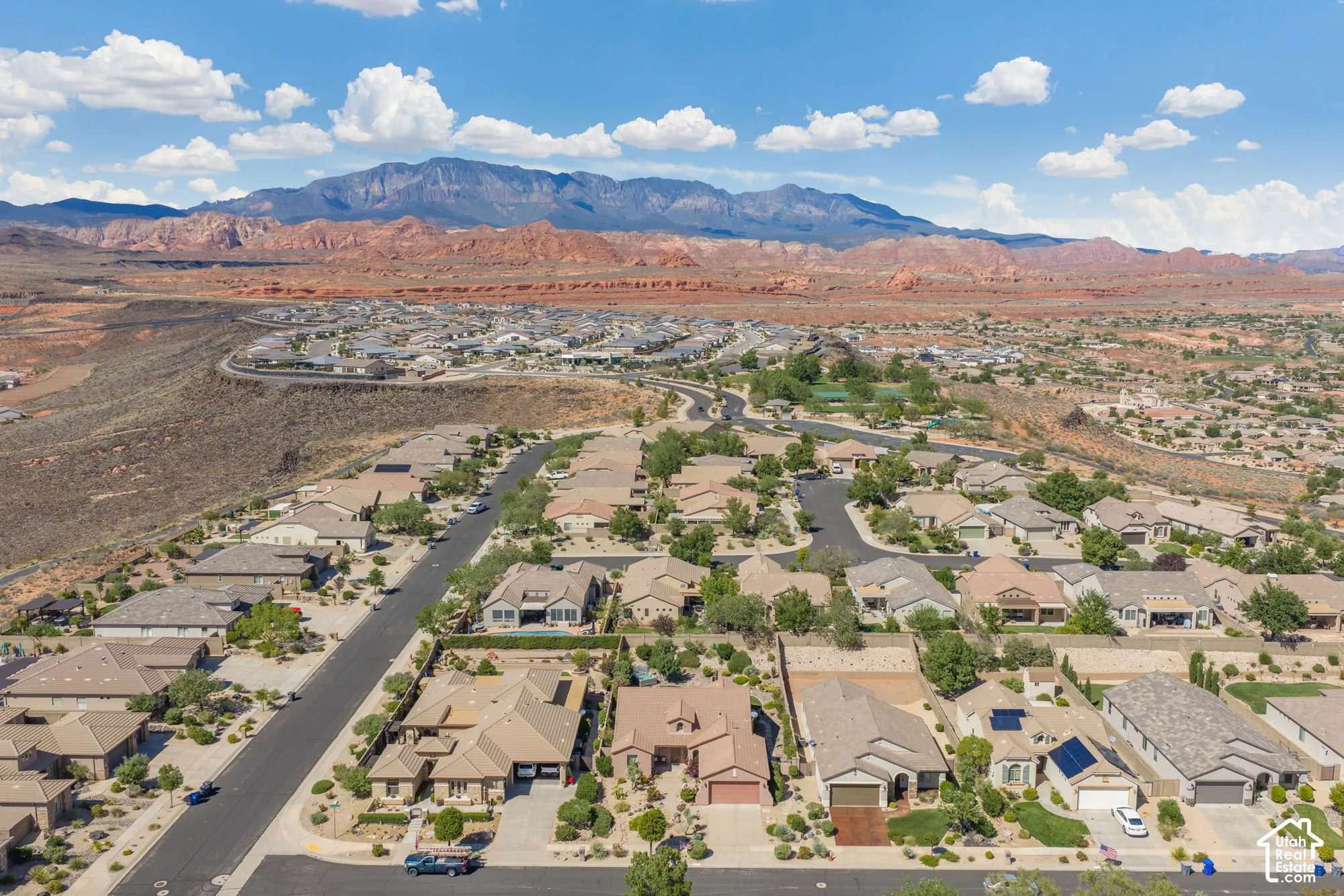 Residential neighborhood with paved streets and mature landscaping, set against a backdrop of distant mountains and red rock formations