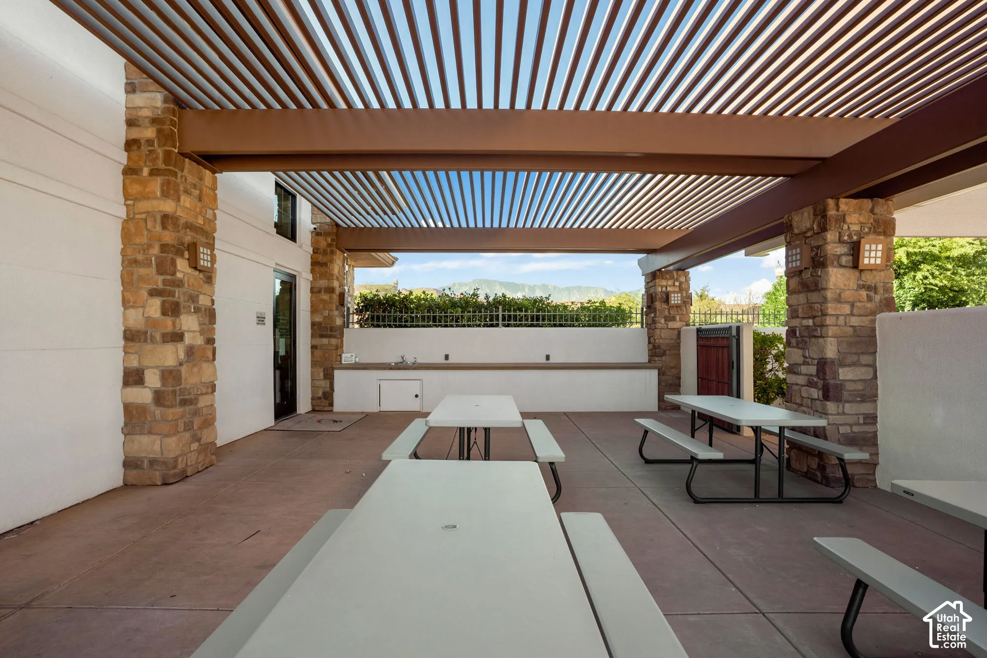 Covered outdoor patio with a slatted roof structure, stone-clad columns, and a built-in counter with sinks