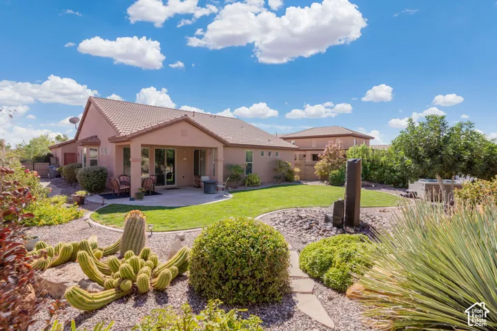 Expansive backyard featuring a manicured lawn, established desert landscaping with stone pathways, and a covered patio area with a concrete surface