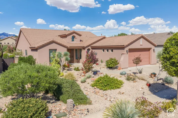 Stucco exterior with a tile roof, desert landscaping, attached two-car garage, and a covered entry