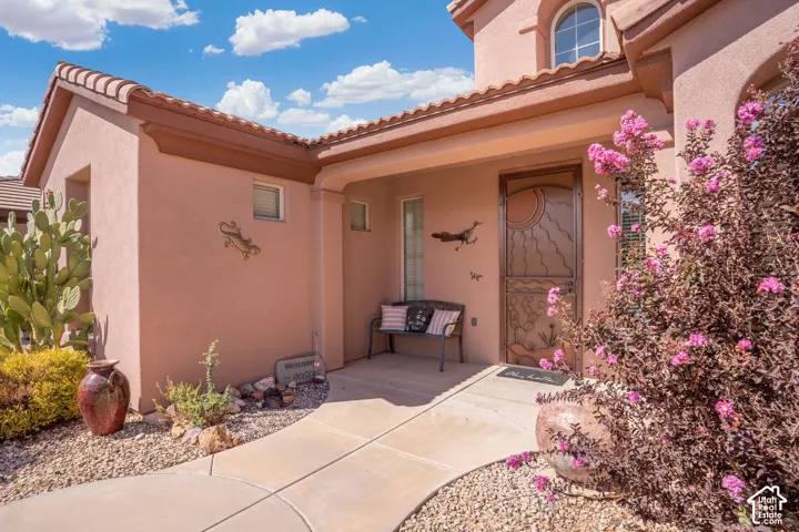 Stucco exterior with a tiled roof, covered entry, decorative security door, and desert landscaping