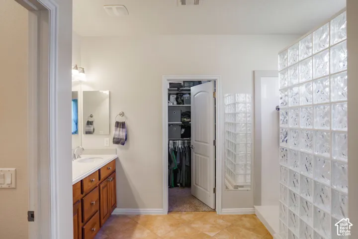 Light-toned tile flooring, wood-finish vanity with countertop, glass block shower enclosure, and recessed lighting