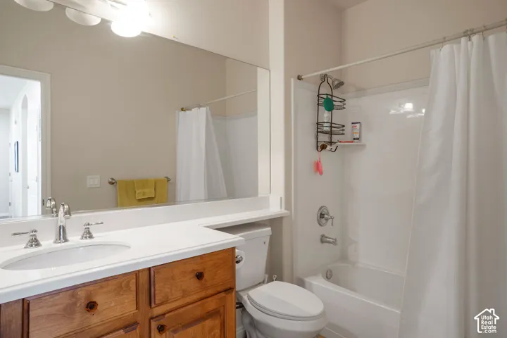Wood-finish vanity with an integrated sink and chrome faucet, white countertop, large wall-mounted mirror, and a full-size bathtub with a shower