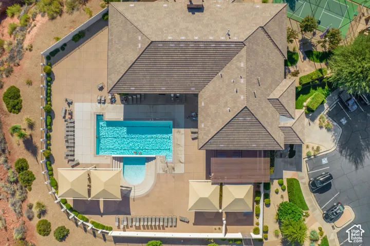 Community building with a multi-level roofline, large rectangular pool, adjacent circular spa, extensive surrounding patio, and dedicated parking