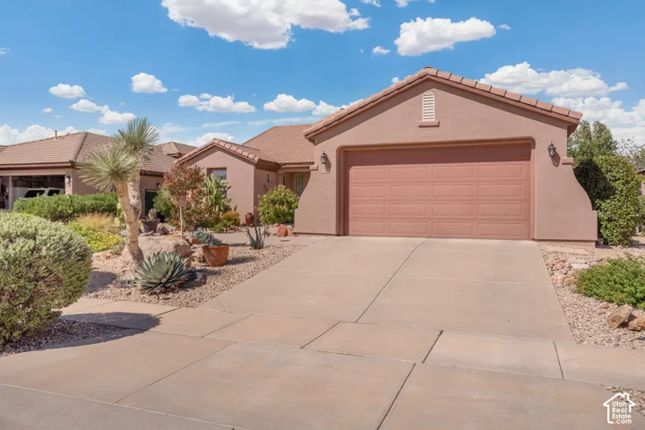 Stucco exterior with a tiled roof, concrete driveway, attached garage, and xeriscaped front yard