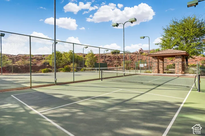 Multiple hard surface courts with chain-link fencing, featuring overhead court lighting