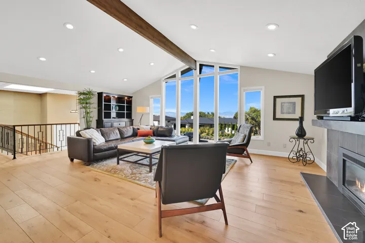 Vaulted ceiling with exposed wood beam, recessed lighting, expansive floor-to-ceiling windows with amazing sunset views, new LVP flooring, and a fireplace with a stone surround