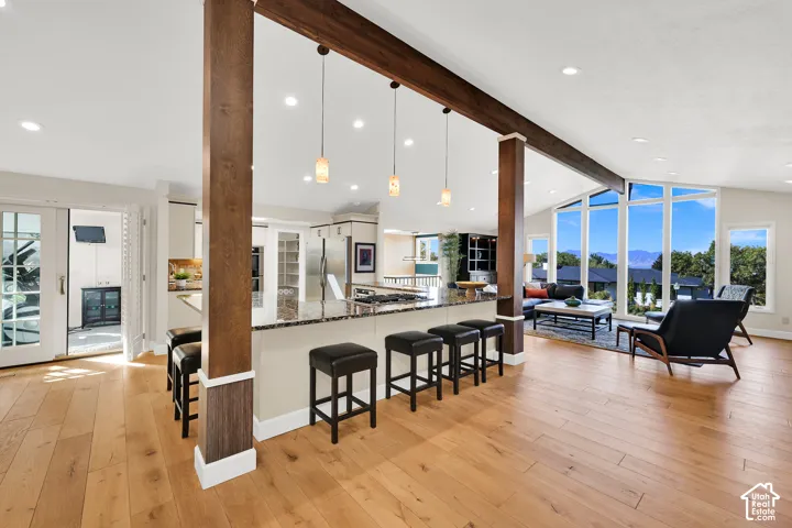 Expansive open-concept space featuring wood-finish flooring, exposed wood beams, a kitchen island with built-in cooktop, and large windows with mountain scenery