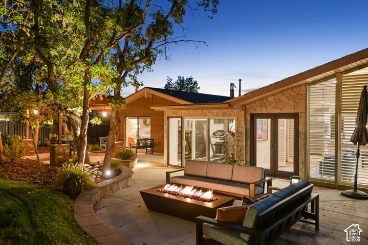 Expansive patio with stone retaining wall, built-in fire pit, multiple glass panel doors, and large windows with horizontal blinds