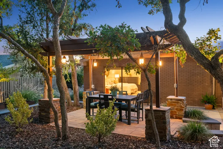 Expansive outdoor patio with pavers and a pergola, featuring built-in lighting and stone-clad columns