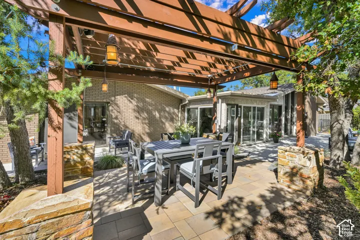 Expansive paver patio featuring a wood pergola with integrated lighting, natural stone columns, and surrounding landscaping