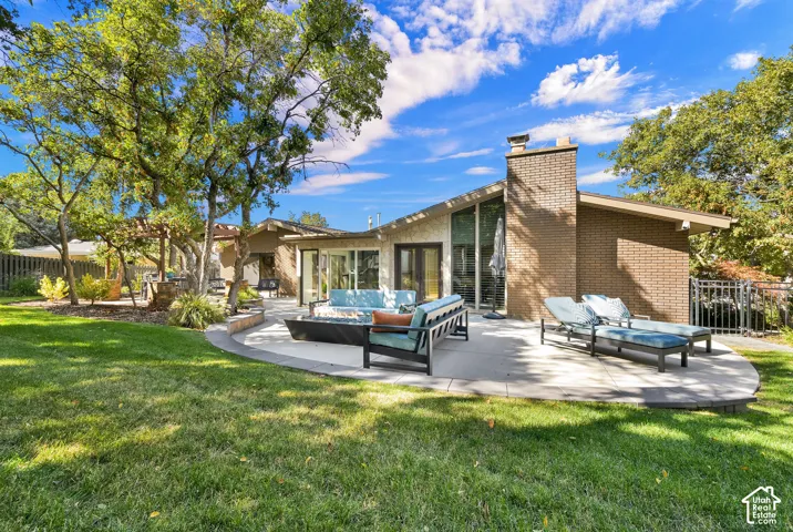 Expansive lawn with mature trees and a curved patio featuring a built-in fire feature