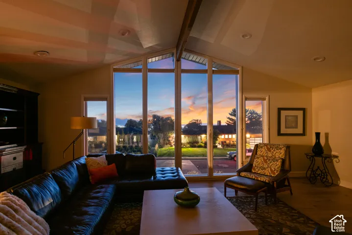 Vaulted ceiling with exposed beam, expansive window wall, additional window, recessed lighting, and wood-finish flooring