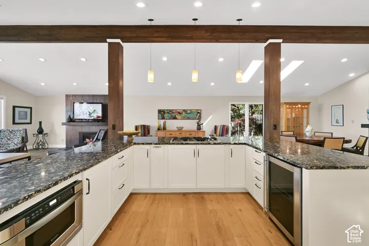 U-shaped kitchen with white cabinetry and dark stone countertops, featuring wood-finish flooring and recessed lighting