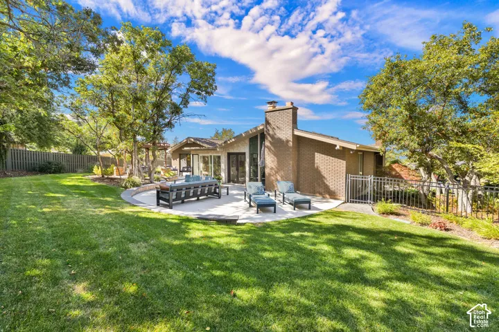 Expansive backyard featuring a large concrete patio, mature trees, a brick exterior, and fully fenced