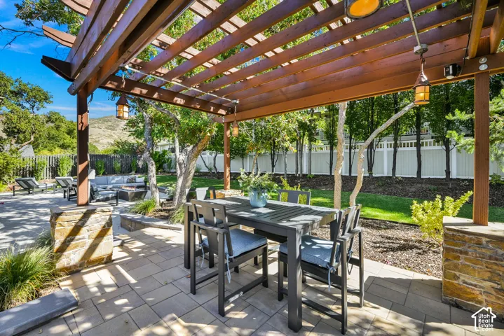 Spacious patio featuring a wooden pergola with pendant lighting, stone accent pillars, and a built-in fire pit area