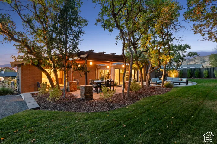 Expansive backyard featuring a manicured lawn, established trees, and multiple paved patio areas