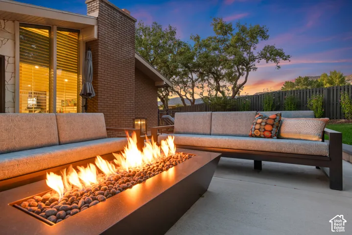 Outdoor patio featuring a rectangular fire pit with river rock accents, brick exterior, and a privacy fence