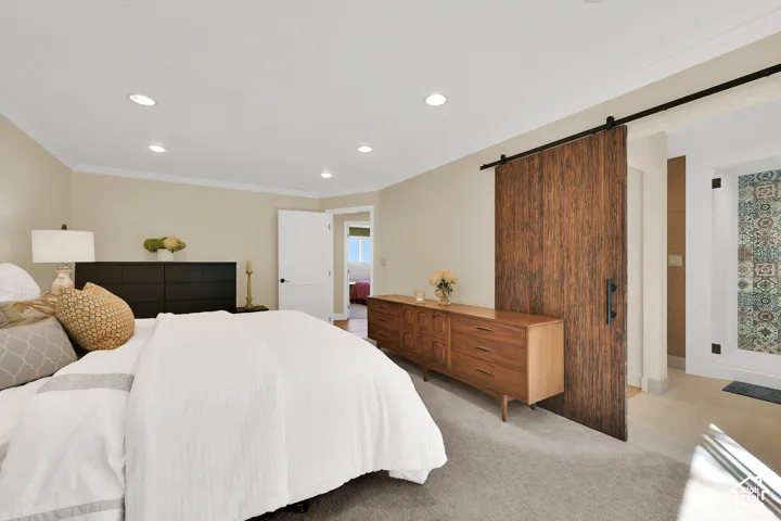 Recessed lighting, crown molding, wood-finish barn door, light-toned carpeting, and a neutral wall color